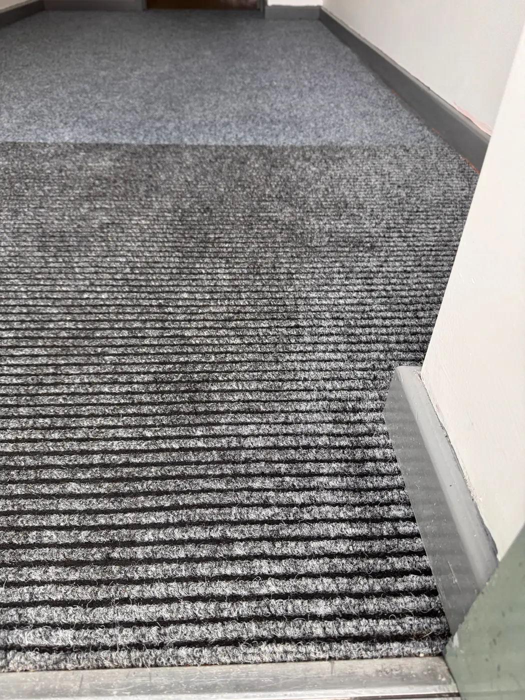 The same grey ribbed entrance carpet after cleaning, with the leaves and debris removed