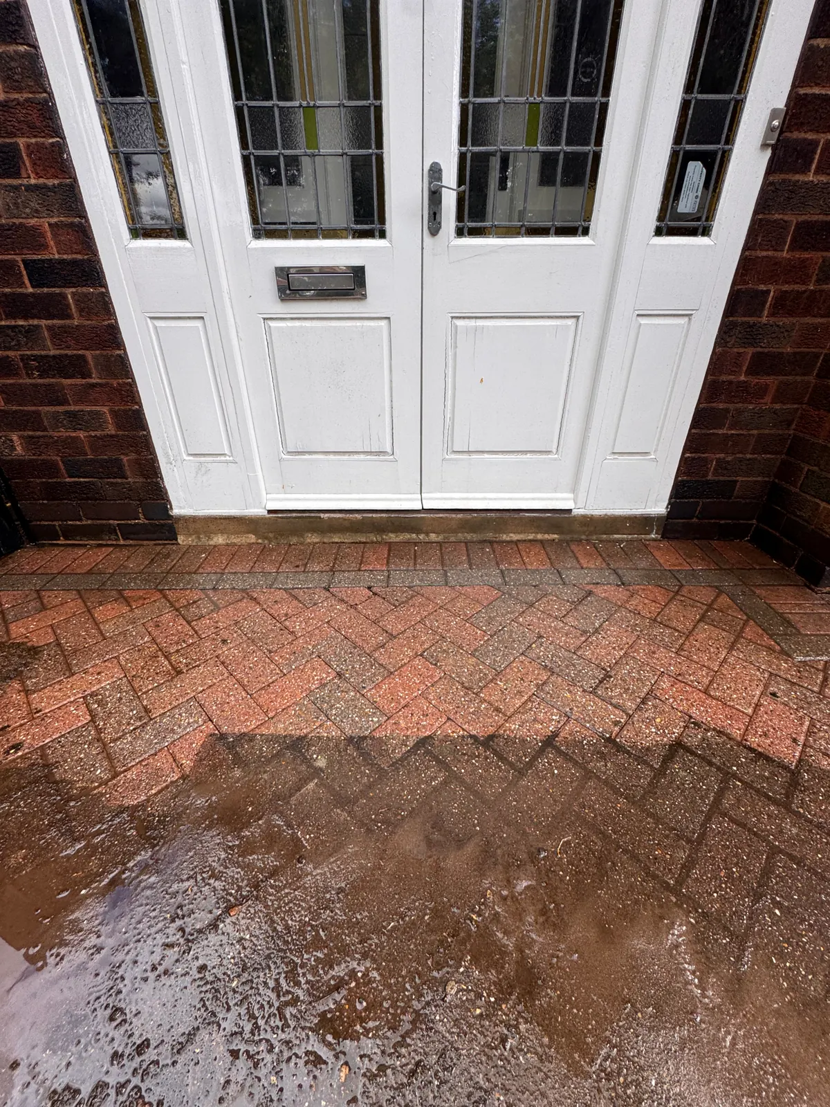 Wet brick paving outside a white front door during exterior cleaning